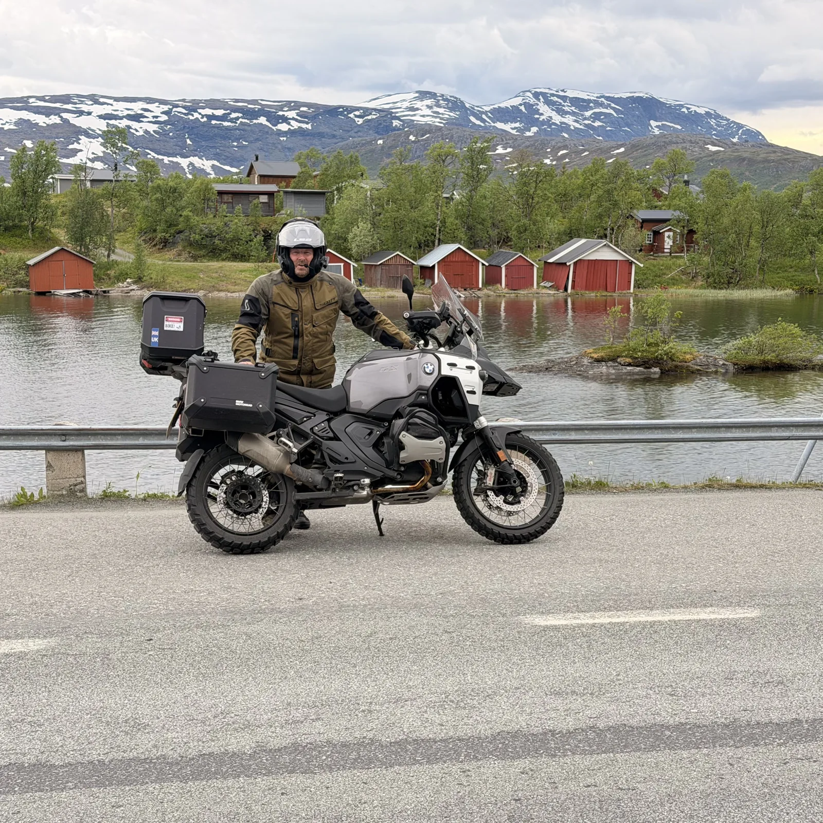 James with his motorcycle beside a Norwegian lake and snowy mountains